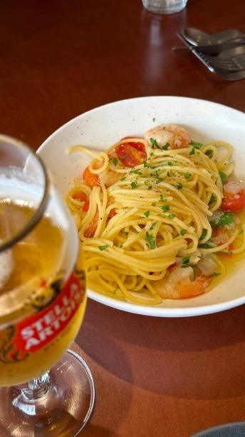 エビとミニトマト、緑の野菜を合わせたオイルパスタ。手前にはビールのグラス