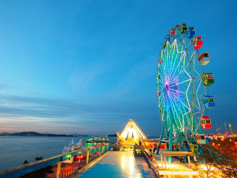 観覧車やレトロなアトラクションが並ぶ月尾島の海辺の遊園地の夕景