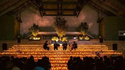 無数のキャンドルの灯りに囲まれた暗いホールで、演奏者たちが弦楽器を弾いている様子