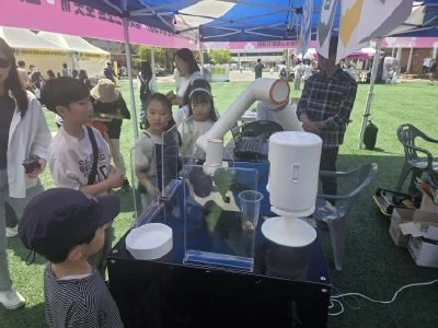 テントの下でロボットアームの装置を子どもたちが囲んで見ているブース
