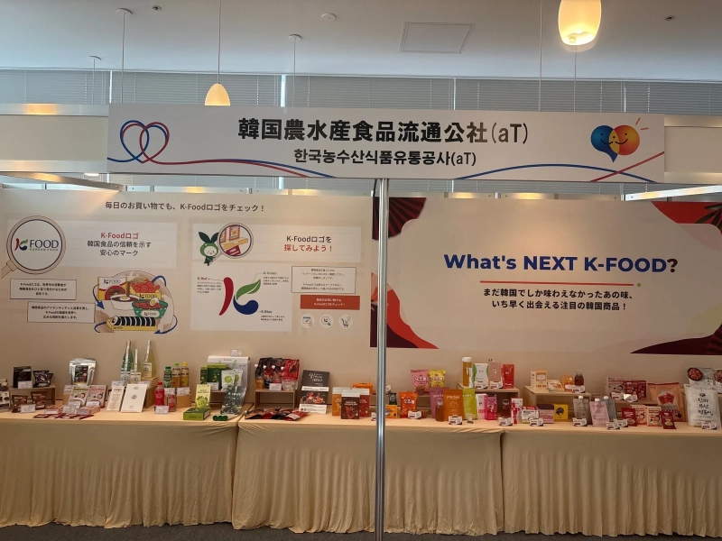 「韓国農水産食品流通公社(aT)」の看板の下に、韓国食品がテーブルいっぱいに並ぶブース