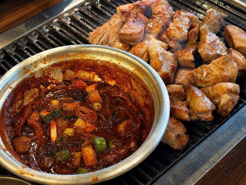 焼き網のとなりで煮えているイワシのたれの小鍋と、焼かれている豚肉